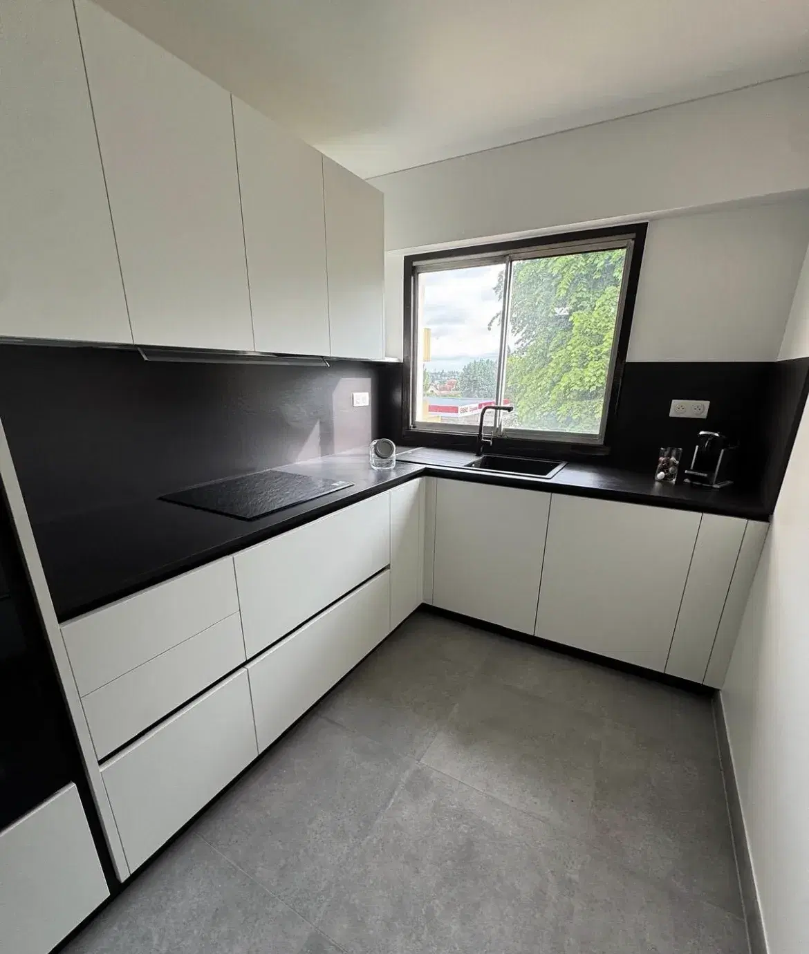 Cuisine rénovée par RENOVLUX : façades blanches sans poignée, plan de travail et crédence noirs