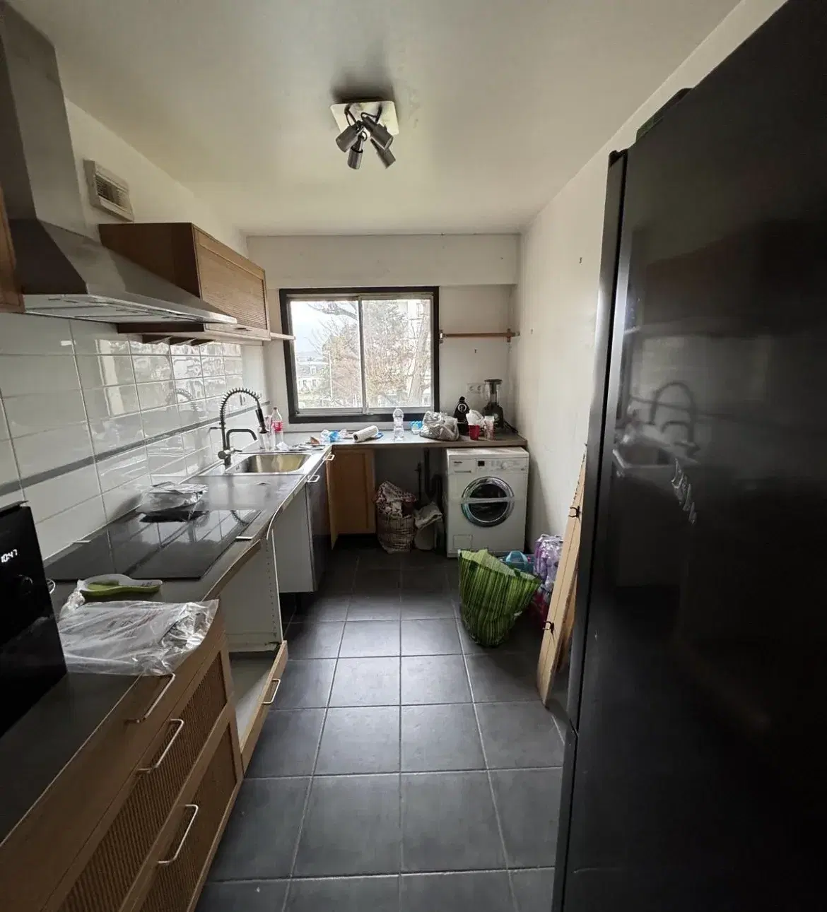 La cuisine avant travaux : meubles en bois, crédence carrelée blanche et carrelage anthracite